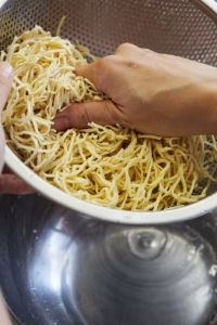 豆腐干をざるに上げて水気をきり、手でぎゅっと押さえつけるようにして水気をしっかりきる。