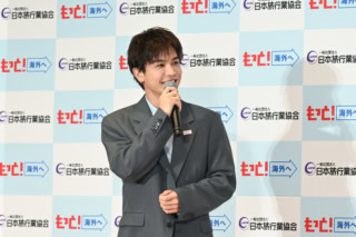 胸元には「もっと！海外へ」のピンバッチがキラリ
