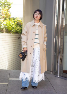 デニムパンツにコットンレースのスカートを重ねた印象的なカジュアルコーデは、トレンチコートと眼鏡でトラッド&きちんと感をプラス。華奢なフレームが奥行きのある重ね着に程よいヌケ感を。