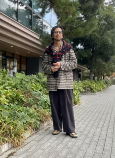 インカミングのエディフィス別注コート、古着のニットとベルト、エディフィスEレーベルのパンツ、肩にかけたガンジウレンスのニット、バディ オプティカルのメガネ、パラブーツのシューズは内田さんの私物