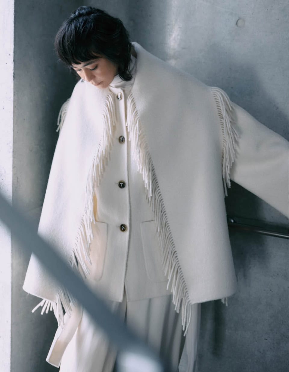 フリンジがポイントになったケープ付きコートを主役に、ワントーンでまとめてクリーンに。落ち感のある素材のパンツを合わせ、軽やかさはキープ。ありそうでない、コンテンポラリーなデザインが目を引く。コート¥229,350、パンツ¥83,050（共にトーテム／トーテム クライアントサービス）