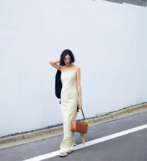 ドレス¥72,600、パンツ¥55,000、手に持ったジャケット¥96,800、バッグに巻いたスカーフ¥16,500、サンダル¥48,400（全てオーラリー）、バッグ¥81,400（オーラリー メイドバイ アエタ／オーラリー）